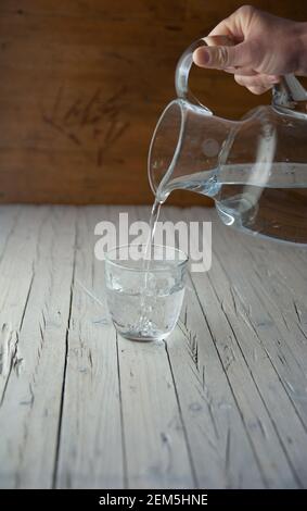 la mano versa una caraffa d'acqua in un bicchiere di vetro Foto Stock