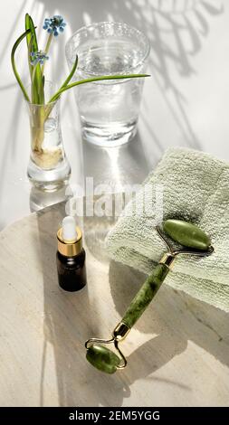 Rullo facciale in quarzo rosa cristallo, pietra di Gua sha per il massaggio del viso. Prodotti e oli rosa per la cura della pelle. Marmo bianco e fondo tessile, naturale Foto Stock