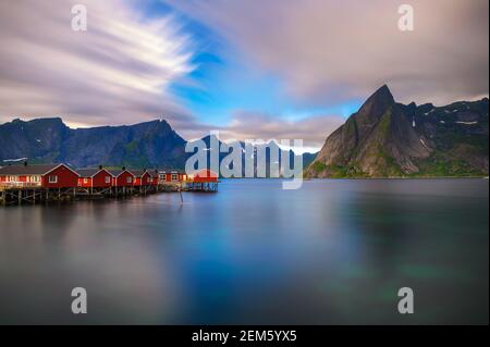 Tramonto sul monte Olstind e cabine di pesca rosse nelle Isole Lofoten, Norvegia Foto Stock