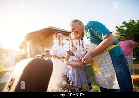 Nonno gioioso e orgoglioso viene baciato su una guancia dalla sua adorabile nipote davanti al resto della famiglia. Foto Stock
