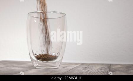 foto: tazzina termica vuota davanti a fondo bianco: polvere di caffè granulare viene versata nella tazza, modio lento Foto Stock