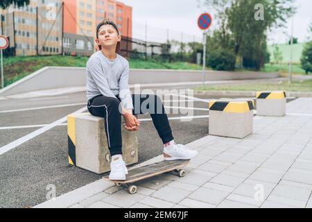 Ritratto di un ragazzo adolescente skateboarder in un cappellino da baseball con vecchio skateboard sulla strada della città. Generazione di giovani tempo libero e una gente attiva Foto Stock