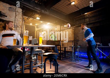 Due tifosi di calcio bassing palla a vicenda utilizzando teste, mentre il terzo ventilatore sta ridendo e bere birra mentre è seduto al tavolo in un pub. Foto Stock