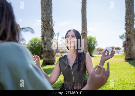 Ritratto di una bella ragazza che pratica lo yoga durante una sessione di gruppo in un parco con palme. Foto Stock