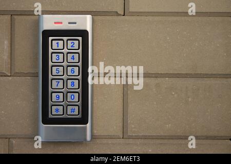 Pannello di chiamata intercom argento con tasti numerici blu, su una colonna recinzione in mattoni beige di una casa privata Foto Stock