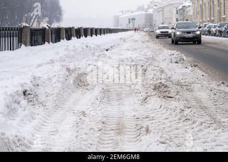 Strada non pulita con nevicate pesanti dopo nevicate in città, auto sulla strada sullo sfondo Foto Stock