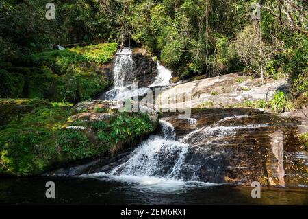 Cascata di Ipiranguinha con la sua corrente d'acqua che scorre intorno formazioni rocciose e la creazione di una piscina naturale dorata proprio sotto nel Densa Serra do Mar Foto Stock