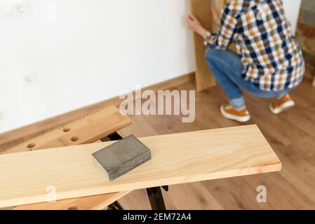 Primo piano di una carta vetrata di legno su un banco da lavoro con una donna che lavora sullo sfondo. Ripresa interna. Luce naturale. Foto Stock