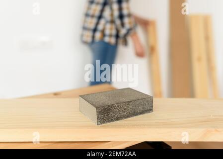 Primo piano di una carta vetrata di legno su un banco da lavoro con una donna che lavora sullo sfondo. Ripresa interna. Luce naturale. Foto Stock