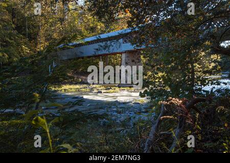 Cleveland, Alabama/USA-Ott 17, 2020: Lunga esposizione del panoramico Swann Covered Bridge retroilluminata dal sole tramontante visto attraverso una pausa nel tr Foto Stock