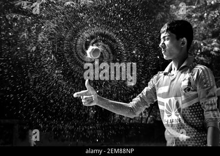 Cumilla, Bangladesh - 24 novembre 2017: Il ragazzo sta spruzzando acqua con una palla di cricket. Bianco e nero Foto Stock