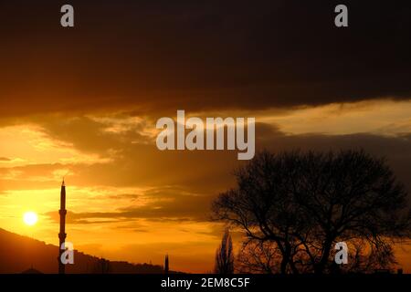 Bursa durante il tramonto con magnifiche nuvole e riflesso del sole sul cielo. Tramonto, uludag, moschea, minareto con pino. Tutte le silhouette in sundown Foto Stock