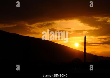 Bursa durante il tramonto con magnifiche nuvole e riflesso del sole sul cielo. Tramonto, uludag, moschea, minareto con pino. Tutte le silhouette in sundown Foto Stock