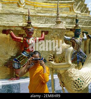 Asia, Thailandia, Bangkok, giovane monaco buddista thailandese che scatta foto di una statua femminile di aspara nel tempio di Wat Phra Kaew Foto Stock