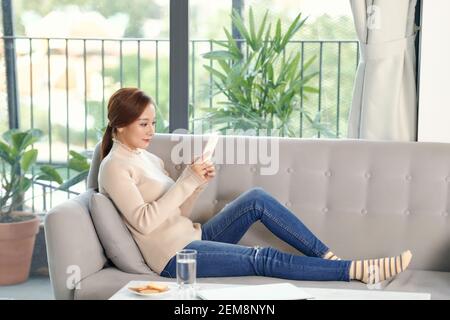 Felice ragazza millenaria che controlla i social media che tengono uno smartphone a casa Foto Stock