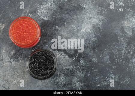 Lastre di vetro piene di caviale rosso e nero su a. sfondo in marmo Foto Stock