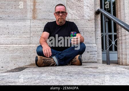 Berlino, Germania, Ritratto di un adulto maturo, maschio caucasico seduto contro una parete grigia. Foto Stock