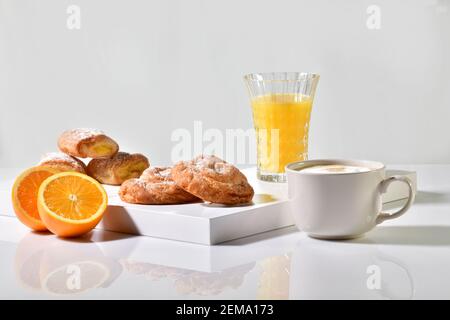 Dolci tradizionali circondati da una tazza di caffè, succo d'arancia e un'arancia tagliata a metà su un tavolo. Concetto di colazione tradizionale. Foto Stock