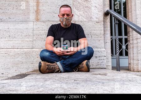 Berlino, Germania, Ritratto di un adulto maturo, maschio caucasico seduto contro una parete grigia. Foto Stock