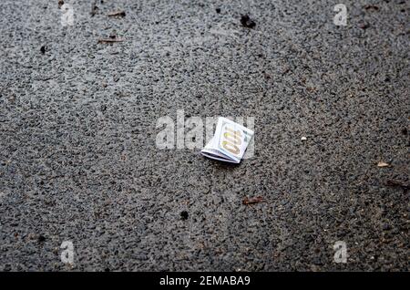 Un disegno di legge di cento dollari crumpled giace sull'asfalto. Denaro perso. Nessuna gente Foto Stock