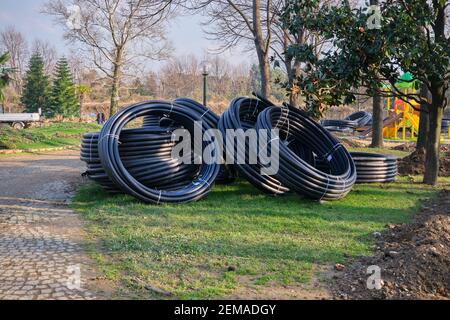 Mazzetto di tubi neri e in plastica in piedi a terra. Tubi per il drenaggio dell'acqua nel parco botanico insieme con sfondo parco giochi Foto Stock