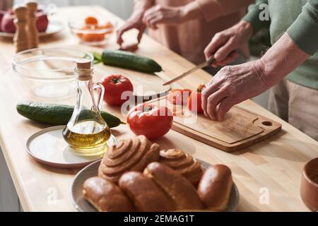 Primo piano di coppia tagliando verdure fresche sul tagliere loro preparazione dell'insalata al tavolo da cucina Foto Stock