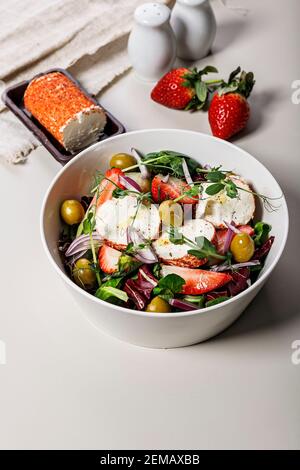 Deliziosa insalata con fragole fresche, cipolle rosse, insalata di ghiaccio, formaggio di capra e olive. Cibo ancora vita su uno sfondo chiaro. Prodotti agricoli biologici. Foto Stock