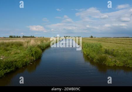 Bella vista di un canale con campi verdi sul lato e un cielo blu con nuvole soffici a Zaanse schans nei Paesi Bassi. Foto Stock