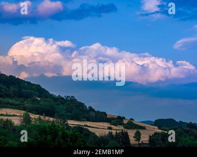 Nuvole massicce che si formano sul cielo blu sopra il paesaggio collinare in prima serata prima del tramonto Foto Stock