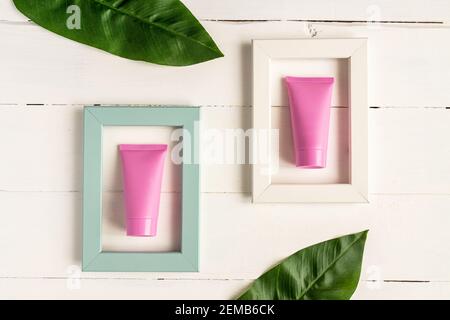 Set di cosmetici per la cura della pelle viso, corpo o mani. Tubi cosmetici bianchi rosa in cornici luminose su sfondo di legno. Concetto di bellezza cosmetica creativa. Foto Stock