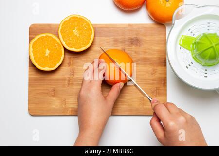 mani che tritano un arancia e uno spremiagrumi Foto Stock
