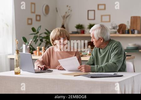 Coppia senior seduta al tavolo con il computer portatile e funzionante con documenti finanziari a casa Foto Stock