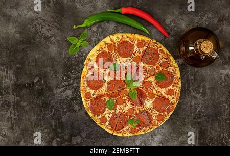 Gustosi pepperoni pizza e ingredienti da cucina, peperoncino, basilico su fondo scuro. Foto Stock