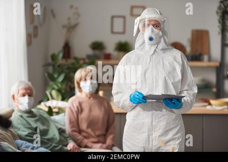 Ritratto di medico in indossare protettivo e maschera guardando fotocamera durante la visita di pazienti anziani a casa Foto Stock