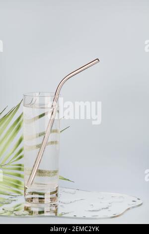 foglia di palma distorto attraverso acqua in vetro con tubo riutilizzabile su sfondo blu. acqua pura, relax, surreale, eco-friendly casa concetto.copia spazio. Foto Stock