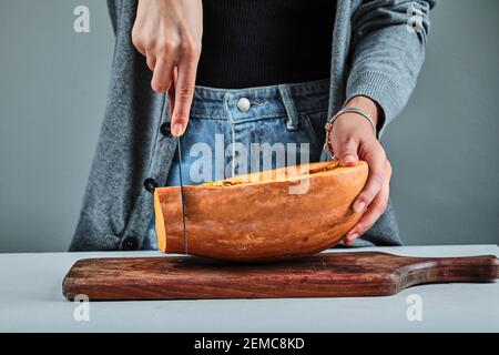 Una mano donna che taglia una fetta di zucca con un coltello sulla tavola di legno Foto Stock