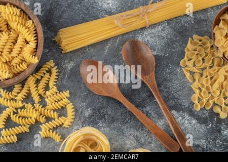 Vari tipi di pasta cruda con cucchiai di legno Foto Stock