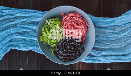 tre deliziose paste, pasta nera, pasta verde e fucsia. piatto grigio su fondo ligneo. Foto Stock