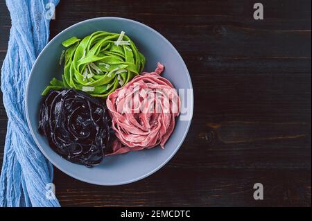 tre deliziose paste, pasta nera, pasta verde e fucsia. piatto grigio su fondo ligneo. Foto Stock