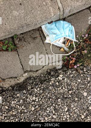 Maschera chirurgica usata gettata via su un lato della strada Foto Stock