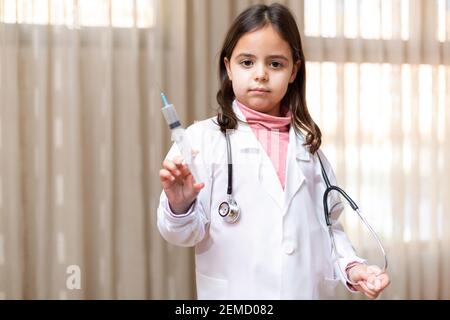 Bambina in uniforme del medico che tiene una siringa in mano. Concetto di salute e benessere. Spazio per il testo. Foto Stock