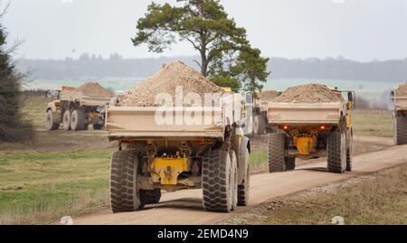 I dumper articolati Yellow Volvo A40E e A40F sparano a terra in un convoglio che fa calciare la polvere mentre attraversano Salisbury Plain, Wiltshire Foto Stock