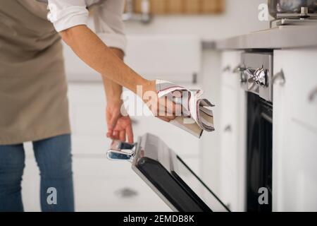 Casalinga in grembiule che apre il forno in cucina Foto Stock