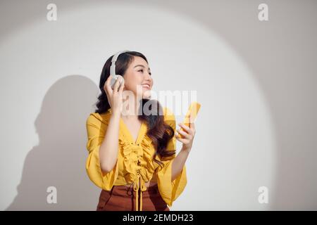 giovane bella ragazza che ascolta la musica attraverso le cuffie e. guardando il suo smartphone su sfondo bianco Foto Stock