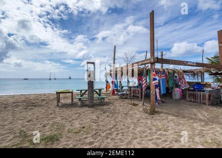 Beach bar, Pinney's Beach sull'isola caraibica di Nevis, abbarbicato in bandiere di fronte ad un mare calmo con yacht ormeggiati sotto un cielo blu e nuvola spia Foto Stock