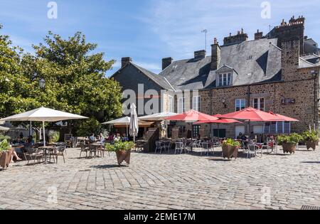 Le persone si rilassano in un caffè all'aperto a Fougeres, in Francia, godendo di un luminoso sole estivo sotto l'ombra di ombrelloni colorati circondati da edifici Foto Stock