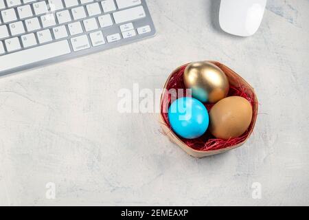 Tastiera e mouse bianchi sulla scrivania con uova colorate nel nido. Pasqua in ufficio. Vista dall'alto Foto Stock