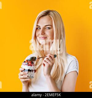 Bella giovane ragazza sana su sfondo luminoso e soleggiato con vasi in mano. In vasi porridge di farina d'avena e muesli con frutti di bosco e cereali Foto Stock