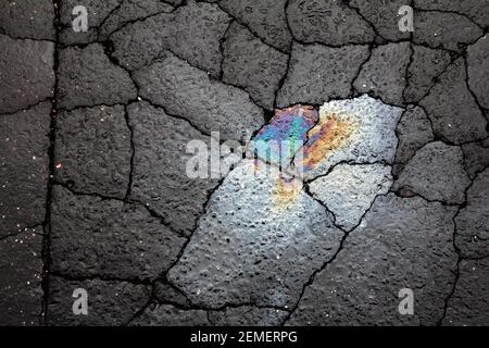 Immagine artistica, astratta ad alto contrasto, con colori arcobaleno fuoriuscita di olio su cemento scuro incrinato su una strada sterrata invecchiata; colore, foto di sfondo. Foto Stock
