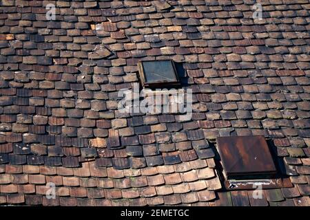 Vecchio tetto, in attesa di ristrutturazione, con tegole in ceramica in cattive condizioni e due lucernari con vetri rotti; foto a colori. Foto Stock